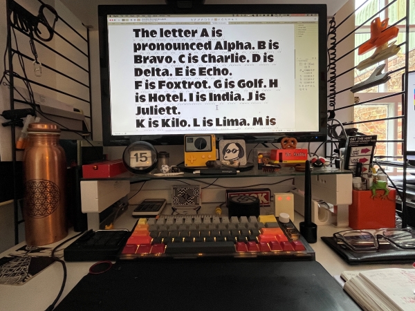 Computer screen with text displayed, as well as a calendar, keyboard, and various desk accessories, following a black, white, orange, red, and yellow color scheme.