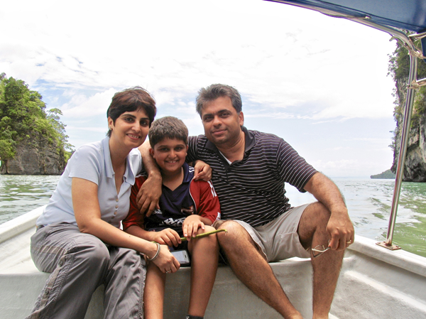 The Gulati family on vacation in Malaysia in 2009. Two parents and child on a boat with trees and water in the background.