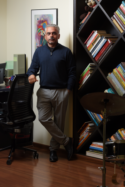 Neeraj Gulati posing for a portrait in front of bookshelves and a drum set.