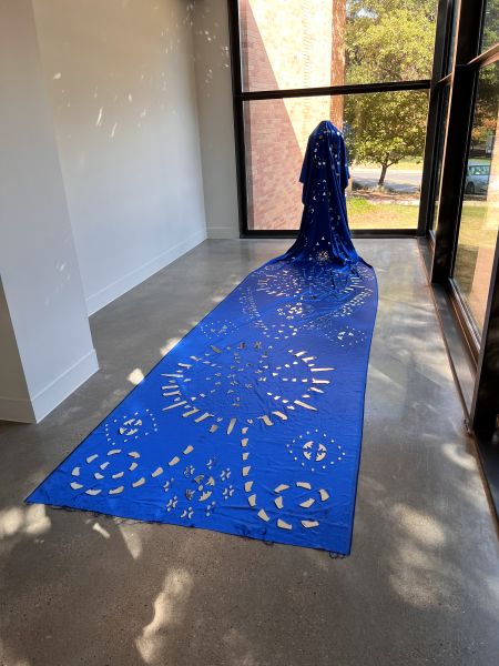 A long, royal blue cape on a mannequin and spread out on the floor. Cuts are taken out in a design.