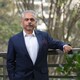 Neeraj Gulati portrait in dark suit, leaning against railing with trees in the background.