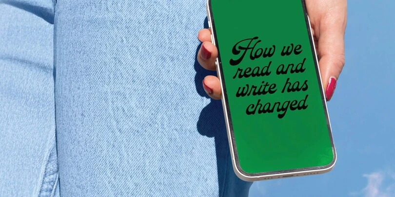 "Hand holding smartphone with green screen displaying 'How we read and write has changed', with denim jeans in background. "Hand holding smartphone with green screen displaying 'How we read and write has changed', with denim jeans in background.